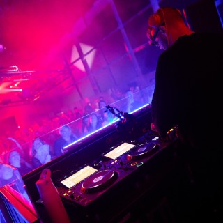 David Puentez performt vor tanzender Crowd in rotem und blauem Licht auf einer Clubbühne.