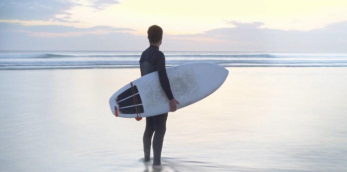 Surfer steht im Sonnenuntergang am Meer – entdecke deinen Alive Moment.