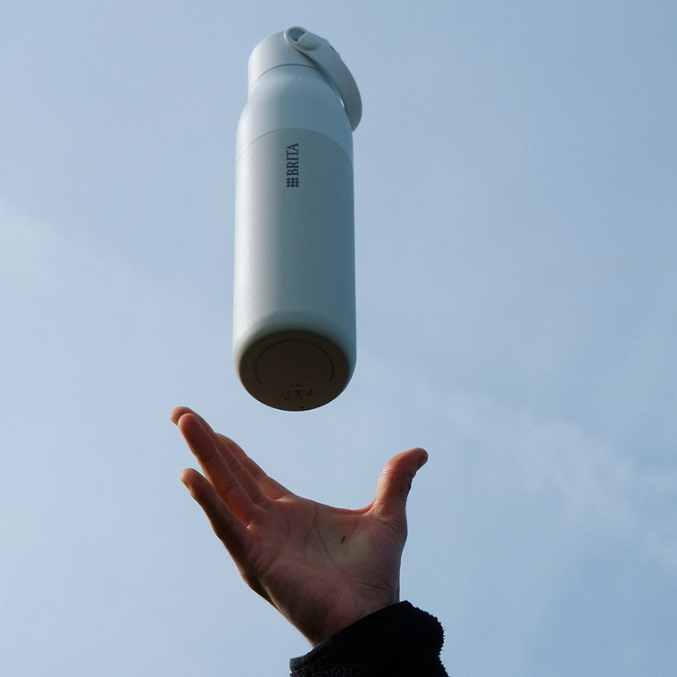 Weiße BRITA LARQ iQ Flasche wird in die Luft geworfen, blauer Himmel im Hintergrund.
