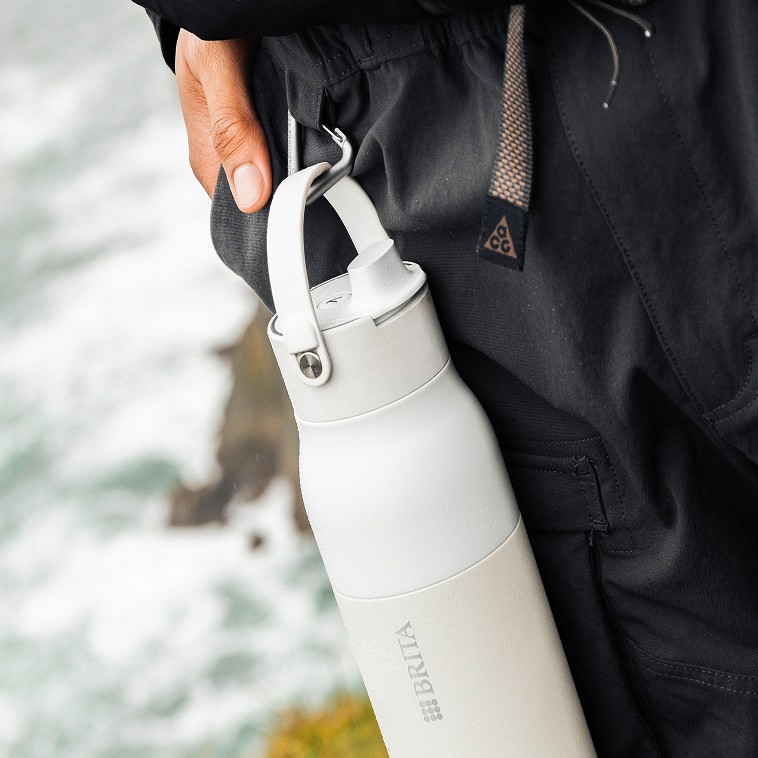 Weiße BRITA LARQ iQ Flasche hängt an einem Karabiner am Rucksack in Outdoor-Umgebung.